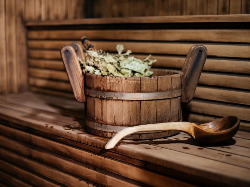 En sauna af træ indefra. Der står en træspand med urter på træbænken med en træske liggen foran