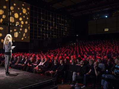 En kvinde står på scenen i Det Kongelige Biblioteks Dronningesal foran publikum.